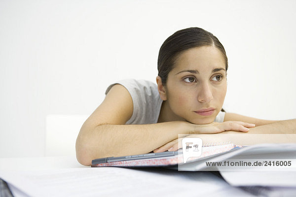Junge Frau sitzend mit Notizbuch  Kopf auf den Armen liegend  wegschauend