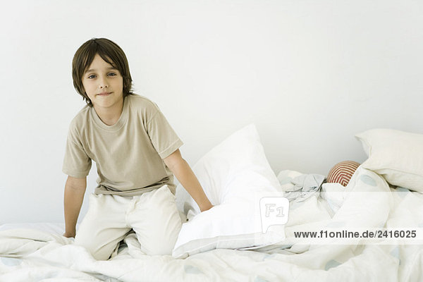 Junge kniend auf ungemachtem Bett  lächelnd vor der Kamera