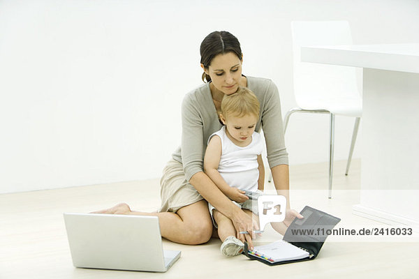 Mother with toddler on lap  looking at agenda  laptop nearby