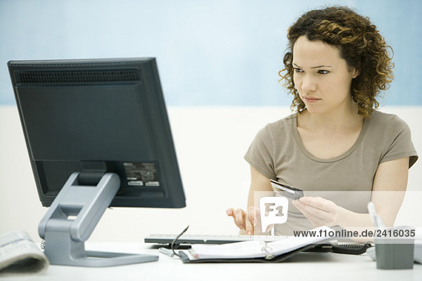 Junge Frau mit Kreditkarte und Blick auf den Computerbildschirm