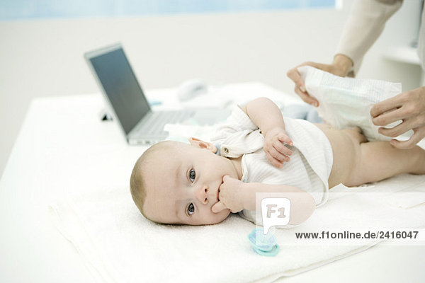 Mother changing baby's diaper on desk  laptop in background