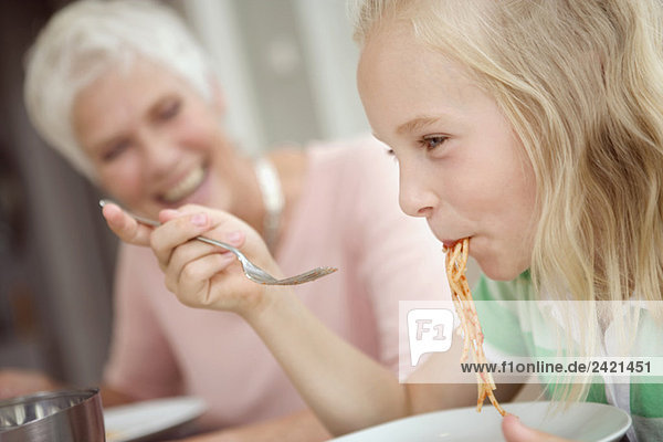 Girl (8-9) eating spaghetti  grandmother in background