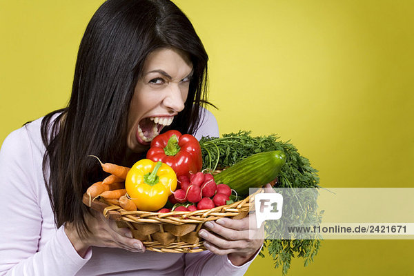 Dunkelhaarige Frau  die einen Korb mit Gemüse hält und herumalbert.
