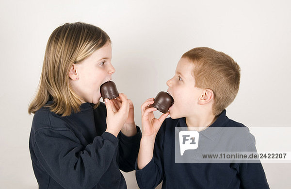 Boy and girl (8-9) eating chocolate marshmallows