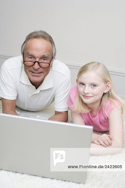 Großvater und Enkelin (8-9) auf dem Boden liegend  mit Laptop  Portrait