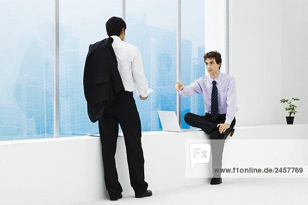 Zwei Geschäftsleute stehen sich gegenüber  einer sitzt auf dem Sims  einer steht.