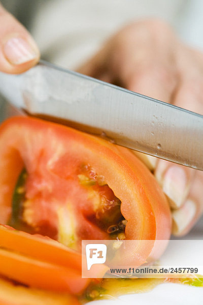 Frau schneidet Tomate mit Messer  abgeschnittene Ansicht der Hand