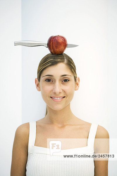 Junge Frau balanciert Apfel mit einem Messer auf dem Kopf  Portrait