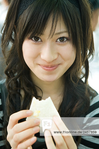 Junge Frau isst Sandwich  lächelt vor der Kamera