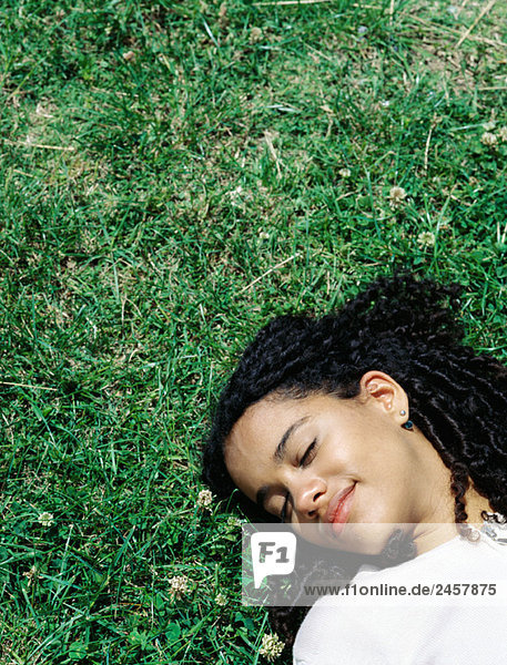 Frau liegt auf dem Rücken auf dem Gras  Kopf und Schultern  Augen geschlossen.