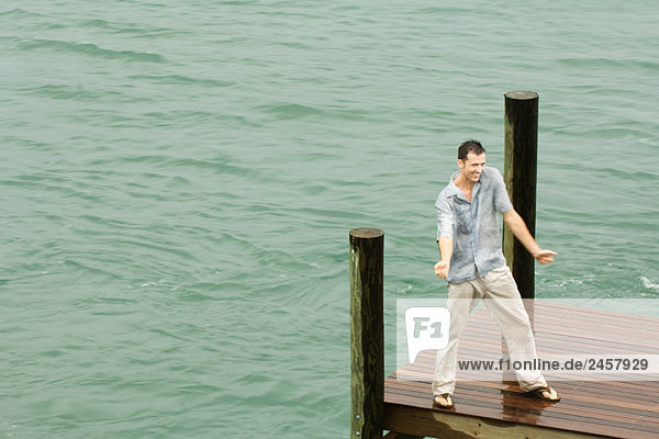 Mann tanzt auf dem Dock  wird nass  Arme ausgestreckt  Hochwinkelansicht