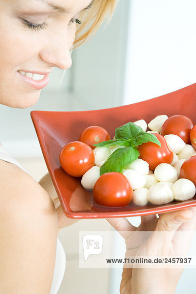 Frau hält Tomaten-Mozzarellasalat hoch  lächelnd  Blick in den Ausschnitt