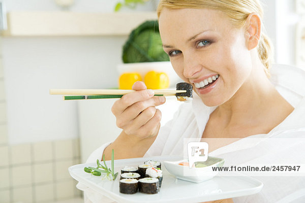 Frau isst Maki-Sushi mit Stäbchen und lächelt in die Kamera.