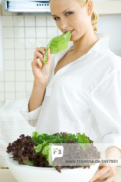 Frau steht vor großer Salatschüssel  isst Salat  schaut in die Kamera