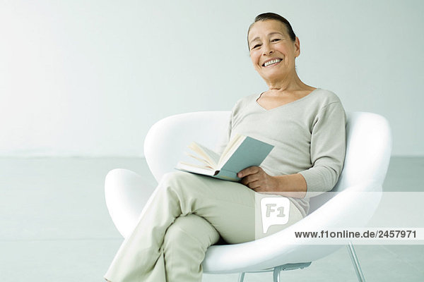 Seniorin im Sessel sitzend  Buch haltend  lächelnd vor der Kamera