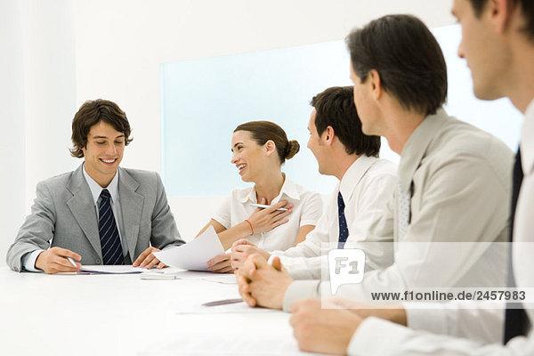 Gruppe von Geschäftspartnern sitzt zusammen am Konferenztisch  Frau lächelt Mann an