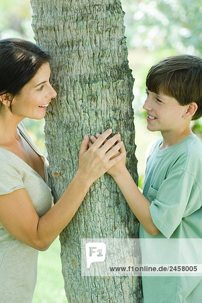 Mutter und Sohn umarmen den Baum und lächeln sich an.