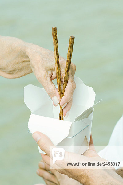Männerhandbehälter  Seniorinnenhand mit Essstäbchen  beschnitten