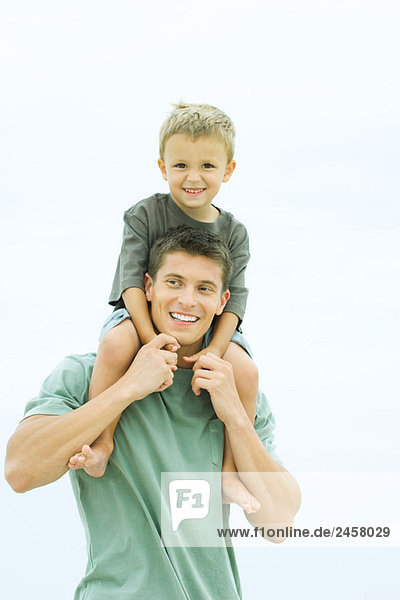 Father carrying son on shoulders  boy looking at camera  both smiling
