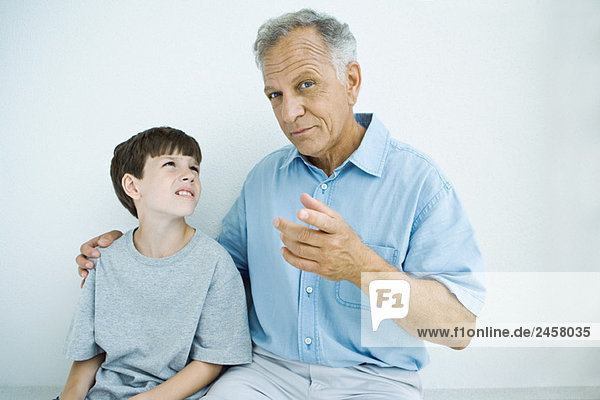 Man sitting with arm around grandson's shoulders  man looking at camera