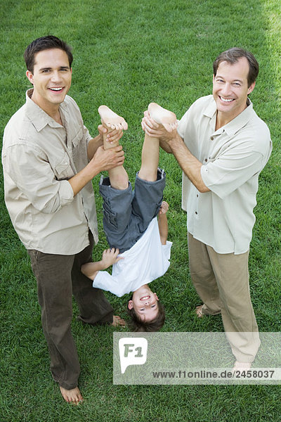 Two men holding little boy upside down by his legs  all smiling  high angle view