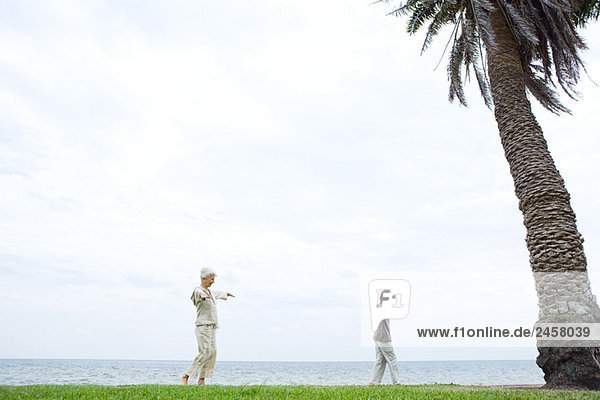Großmutter und Enkel beim Spaziergang am Meer  Arme ausstrecken  Seitenansicht