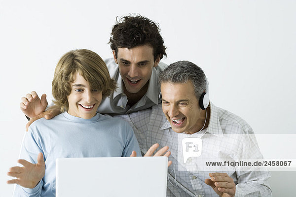 Vater und zwei Söhne schauen gemeinsam auf den Laptop  lächelnd  die Hände erhoben