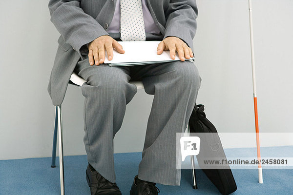 Geschäftsmann im Stuhl sitzend,  weißer Stock neben ihm gestützt,  Dokument haltend,  beschnitten