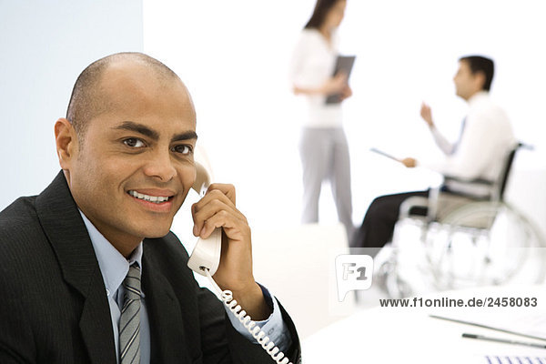 Businessman using phone  smiling at camera  colleagues in background