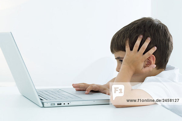 Little boy using laptop computer  holding head  side view