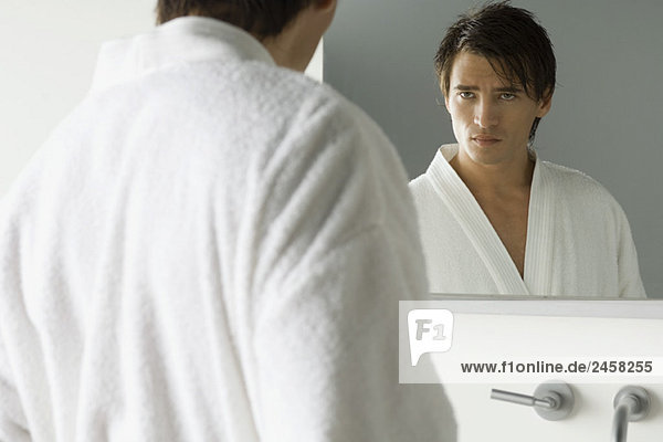 Mann schaut sich im Spiegel an  trägt Bademantel  furchende Braue