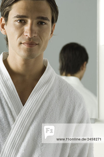 Man wearing bathrobe  smiling at camera  mirror in background