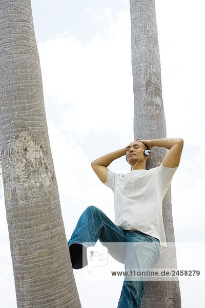 Man leaning against palm tree  eyes closed  listening to headphones