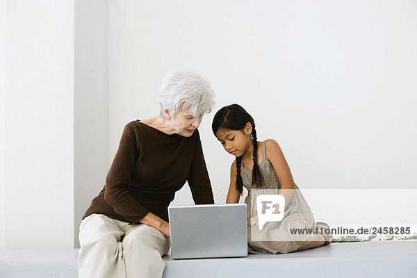 Senior woman and granddaughter using laptop together  looking down