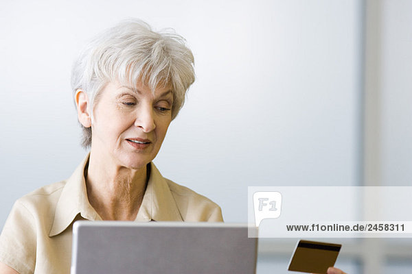 Senior Frau schaut auf Kreditkarte  sitzt hinter dem Laptop