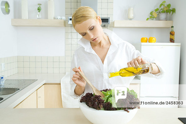 Frau steht in der Küche und gießt Olivenöl über den Salat.