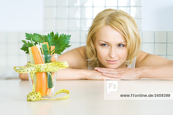 Junge Frau beim Anblick eines Glases frischen Gemüses mit einer Maßband-Schleife