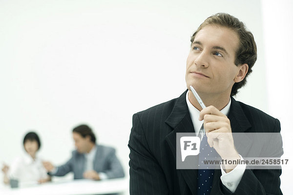 Businessman holding pen against chin  looking up in thought