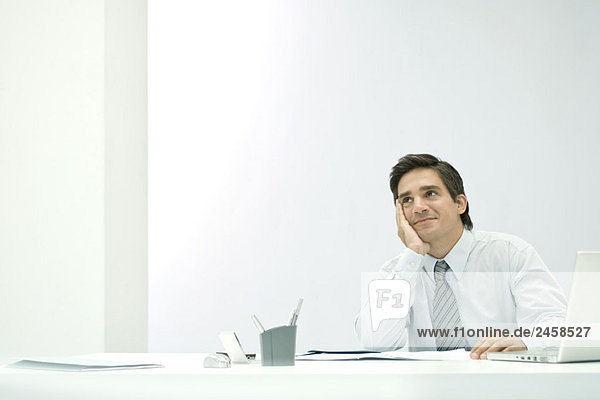 Male professional daydreaming at desk  hand under chin