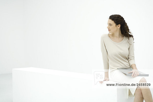 Young female professional sitting on ledge  holding binder  looking over shoulder