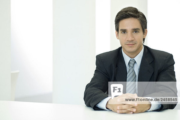 Male professional sitting with clasped hands  looking at camera