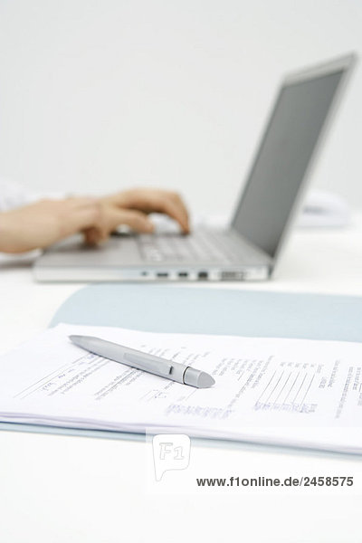 Person mit Laptop-Computer  Ausschnitt  Fokus auf Stift und Dokument im Vordergrund