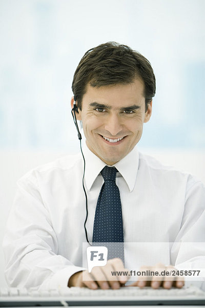 Mann mit Headset und Computertastatur  lächelnd vor der Kamera