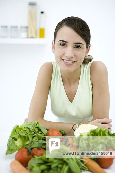Woman leaning behind assorted fresh vegetables  smiling at camera