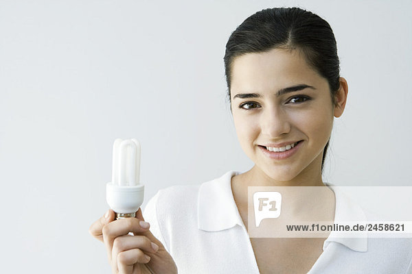 Junge Frau mit Energiesparlampe  lächelnd vor der Kamera