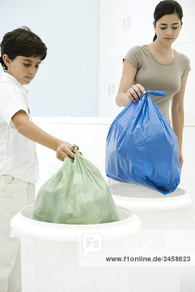 Junge Frau und Junge stellen Müllsäcke in getrennte Mülltonnen