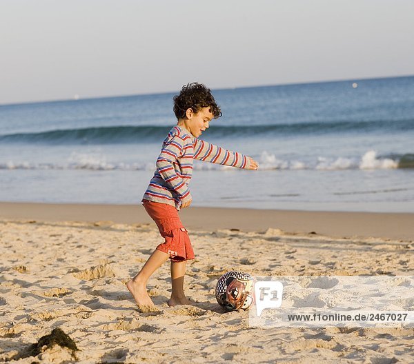 Ein Junge spielen mit einem Ball am Strand Portugal.