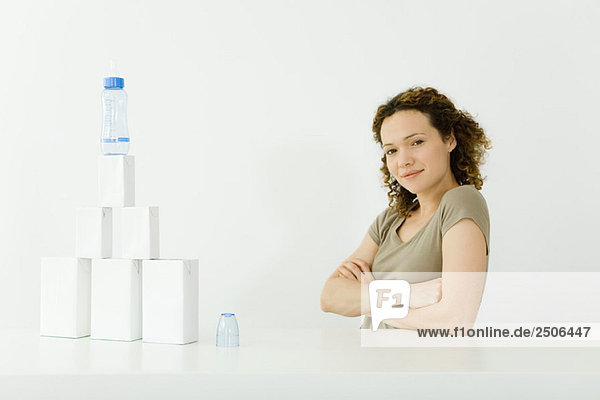 Frau neben gestapelten Milchkartons und Babyflasche  Arme gefaltet  Kamera lächelnd