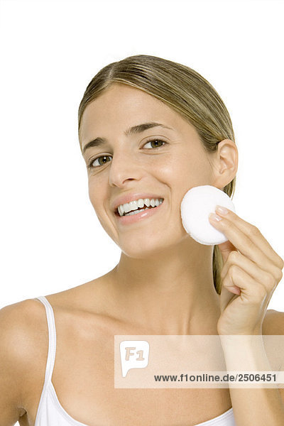 Frau wischt Gesicht mit Baumwoll-Kosmetikpad  lächelnd vor der Kamera