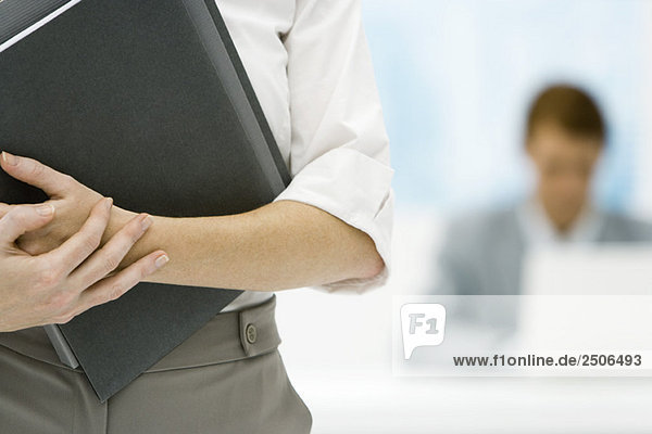 Professional woman holding binder  cropped view  male colleague in background